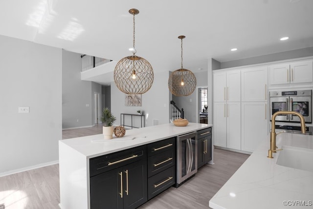 kitchen featuring wine cooler, white cabinets, a sink, and light wood-style flooring