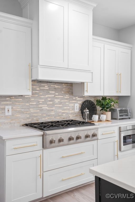 kitchen featuring light wood-type flooring, stainless steel gas stovetop, white cabinets, and backsplash