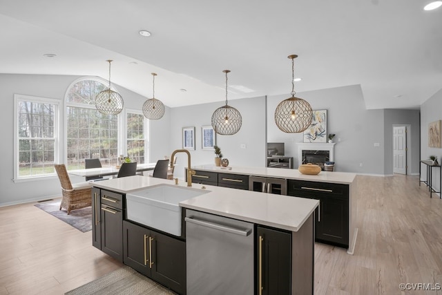 kitchen with stainless steel dishwasher, light wood-type flooring, a sink, and a center island with sink