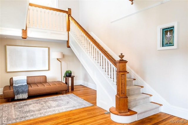 stairs featuring wood finished floors, a towering ceiling, and baseboards