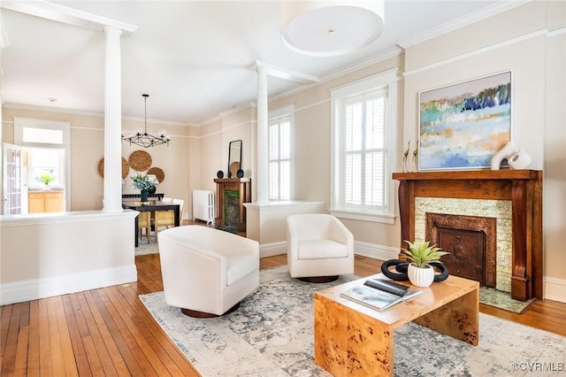 living area featuring decorative columns, baseboards, a tile fireplace, hardwood / wood-style floors, and crown molding