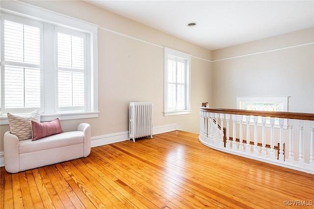 sitting room featuring light wood-style floors, plenty of natural light, visible vents, and radiator