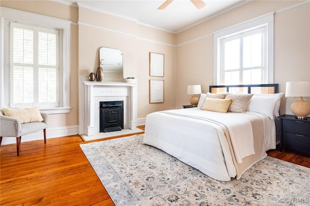 bedroom featuring ornamental molding, a fireplace with flush hearth, ceiling fan, wood finished floors, and baseboards