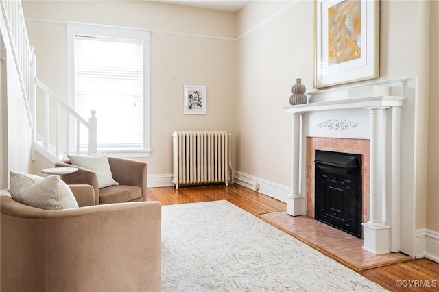 living area featuring radiator, stairway, wood finished floors, a tile fireplace, and baseboards