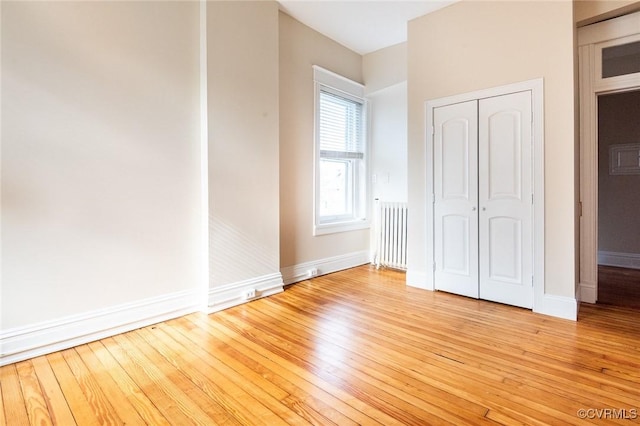 unfurnished bedroom with light wood-style floors, radiator heating unit, a closet, and baseboards