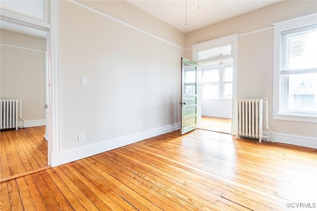 empty room with light wood finished floors, radiator heating unit, and a wealth of natural light