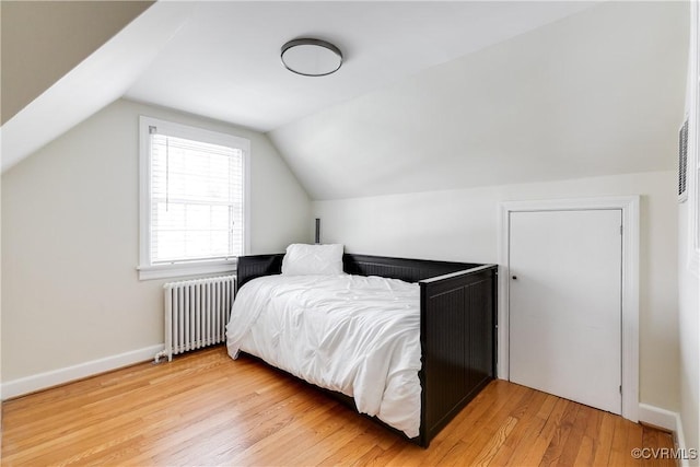 bedroom featuring lofted ceiling, light wood-style flooring, radiator heating unit, and baseboards