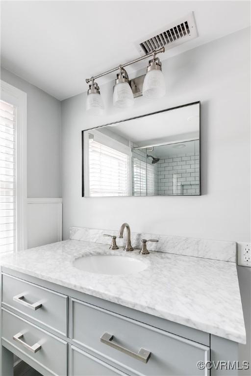 bathroom featuring visible vents, tiled shower, and vanity