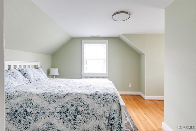 bedroom featuring visible vents, baseboards, lofted ceiling, and wood finished floors