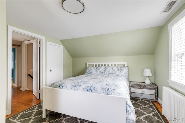 bedroom with visible vents, baseboards, radiator heating unit, lofted ceiling, and wood finished floors