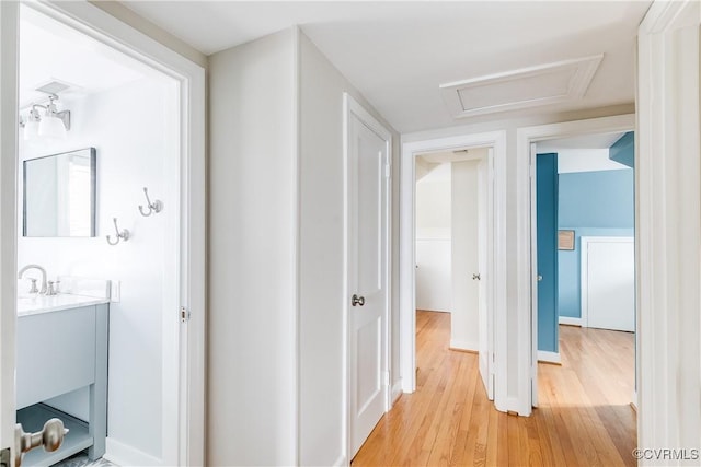 hall with baseboards, attic access, and light wood-style flooring