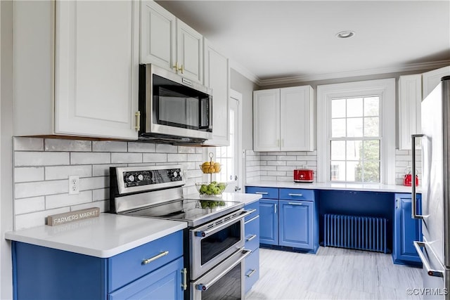 kitchen with blue cabinetry, appliances with stainless steel finishes, radiator heating unit, and light countertops