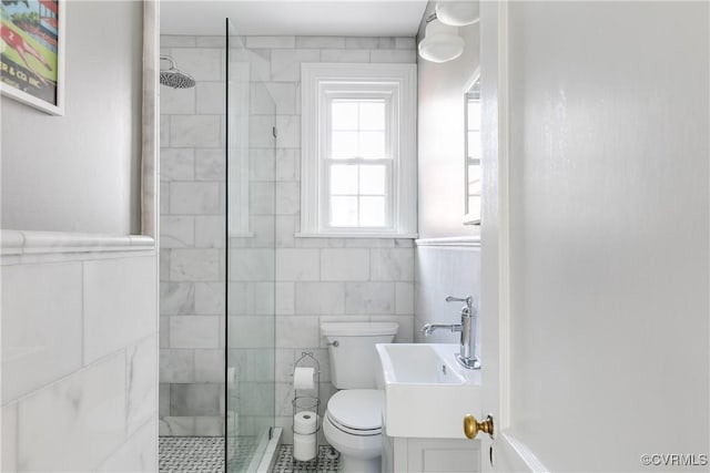 bathroom featuring a wainscoted wall, a walk in shower, toilet, and tile walls