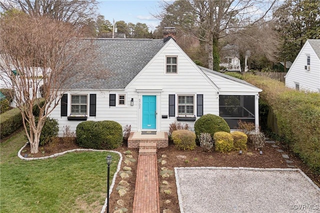 view of front of property with a chimney, a sunroom, a front yard, and roof with shingles