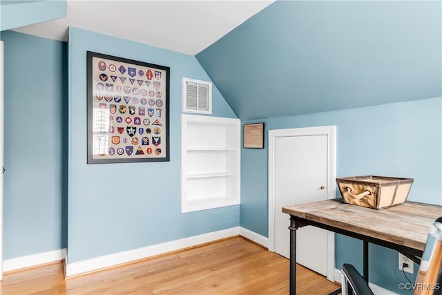 office area featuring built in shelves, visible vents, baseboards, vaulted ceiling, and light wood-style floors