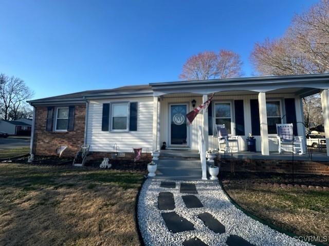 view of front of house with covered porch, brick siding, and a front yard