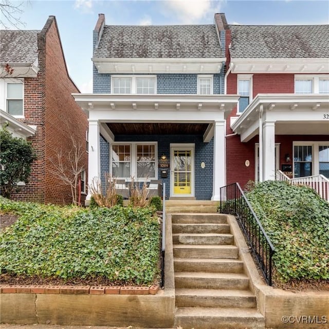 view of front of house featuring a porch, brick siding, and mansard roof