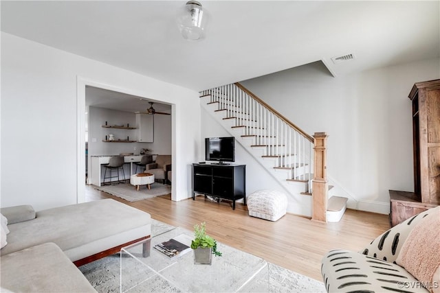 living area with wood finished floors, visible vents, baseboards, a ceiling fan, and stairway