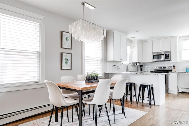 dining area with baseboard heating, an inviting chandelier, and light wood-style floors