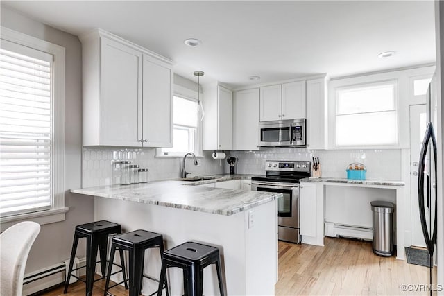 kitchen with a baseboard heating unit, appliances with stainless steel finishes, white cabinets, and a sink