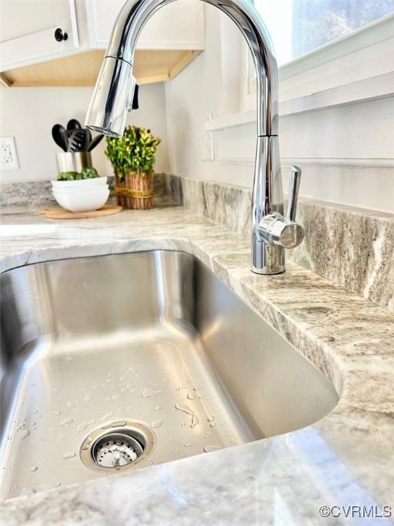 interior details featuring light stone counters, a sink, and white cabinets