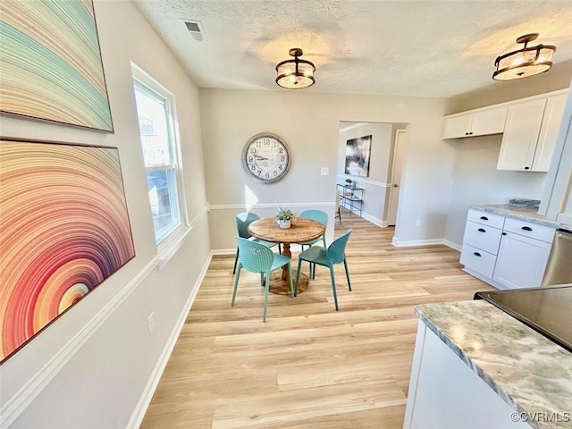 dining room with light wood-type flooring, visible vents, a textured ceiling, and baseboards