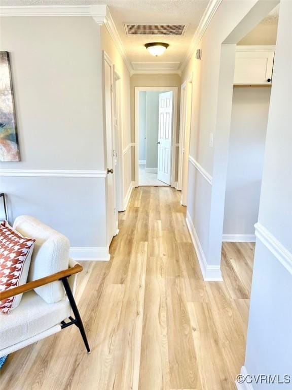 hallway with baseboards, light wood-style flooring, visible vents, and crown molding