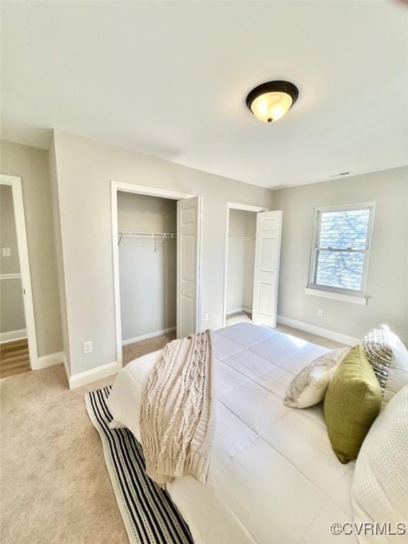 bedroom with carpet floors, baseboards, and two closets