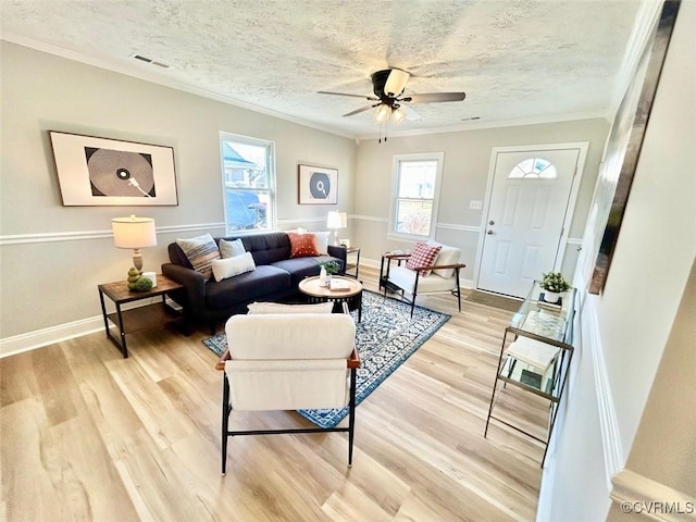 living area featuring light wood-type flooring, visible vents, a textured ceiling, and ornamental molding