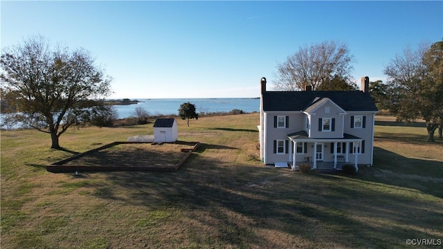 exterior space featuring covered porch, a front lawn, a water view, and an outbuilding