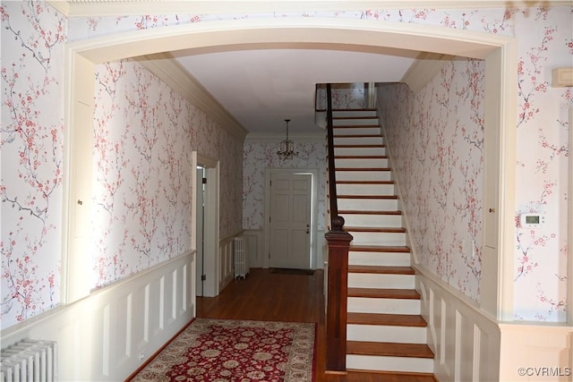 stairway featuring arched walkways, a wainscoted wall, wallpapered walls, radiator heating unit, and crown molding