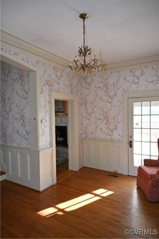 unfurnished dining area featuring wallpapered walls, crown molding, wood finished floors, and wainscoting