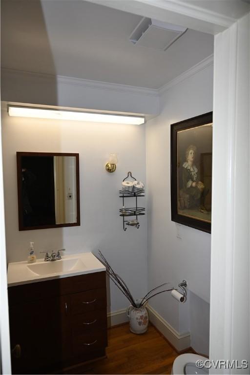 half bath featuring toilet, wood finished floors, vanity, baseboards, and crown molding