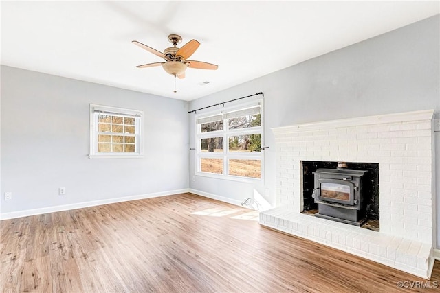 unfurnished living room with plenty of natural light, wood finished floors, a wood stove, and baseboards