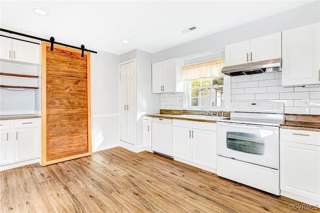 kitchen featuring a barn door, under cabinet range hood, white appliances, a sink, and visible vents