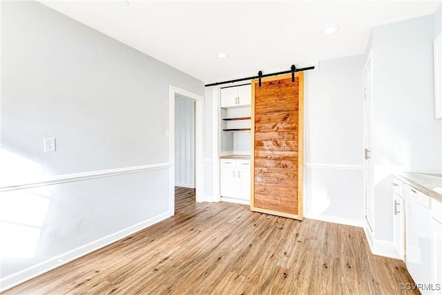 interior space with light wood-type flooring, a barn door, baseboards, and recessed lighting