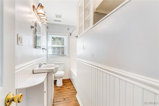 bathroom featuring a wainscoted wall, bathing tub / shower combination, toilet, and wood finished floors