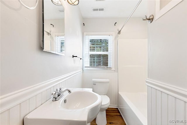 bathroom featuring visible vents, toilet, a wainscoted wall, wood finished floors, and tub / shower combination