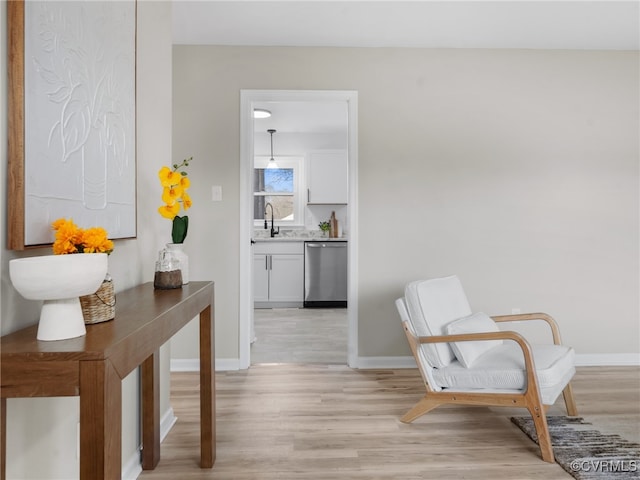 corridor with light wood-style flooring, baseboards, and a sink