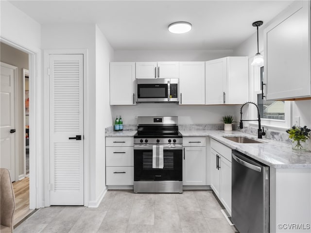 kitchen with light stone countertops, decorative light fixtures, stainless steel appliances, white cabinetry, and a sink