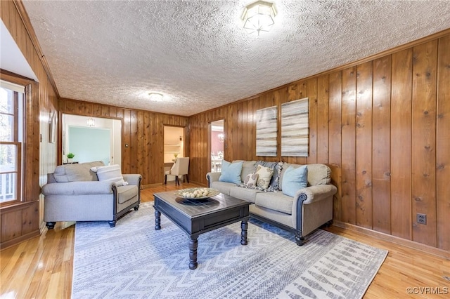 living room with light wood finished floors, wooden walls, baseboards, and a textured ceiling