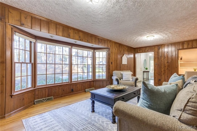 living area with a textured ceiling, wooden walls, visible vents, and light wood-style floors