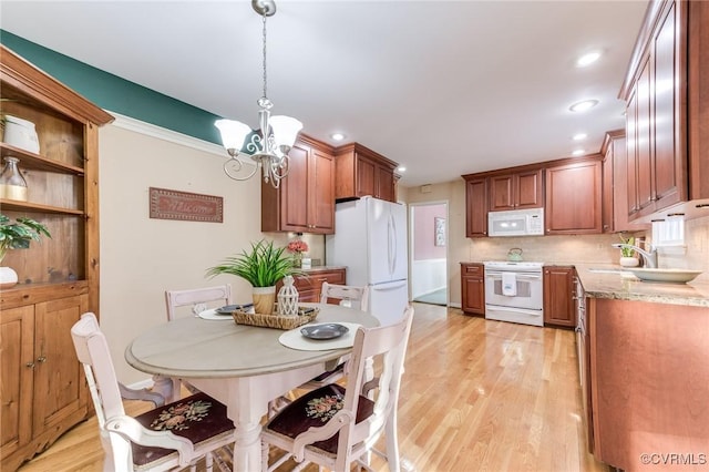 kitchen with white appliances, a chandelier, light wood finished floors, and a sink