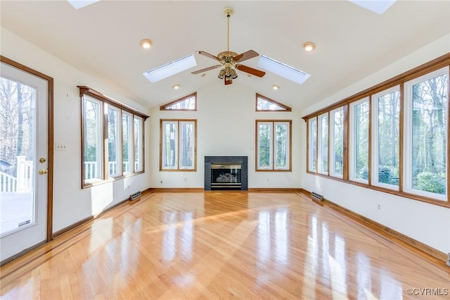 unfurnished living room with a skylight, a glass covered fireplace, light wood-style flooring, and baseboards