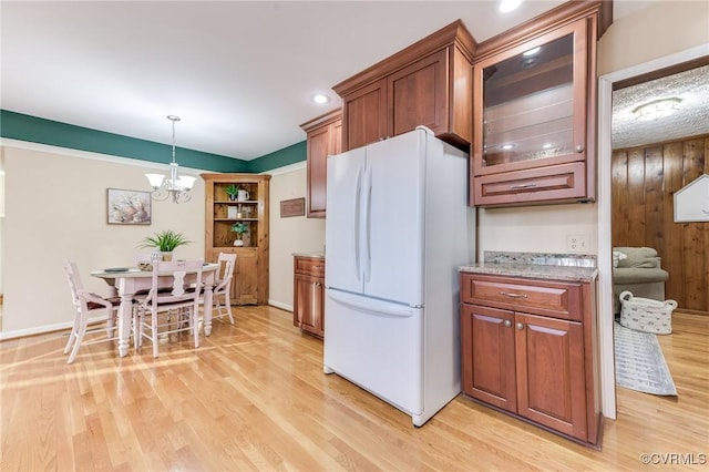 kitchen with brown cabinetry, glass insert cabinets, freestanding refrigerator, light wood-type flooring, and pendant lighting