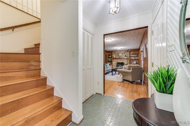 entrance foyer with a textured ceiling, stairway, a brick fireplace, and crown molding