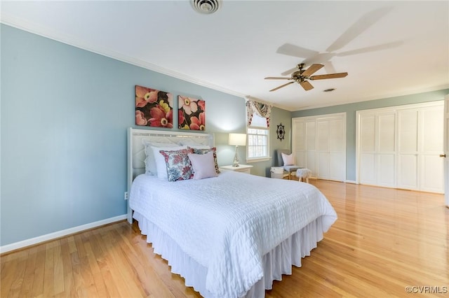 bedroom featuring crown molding, multiple closets, visible vents, light wood-style floors, and baseboards