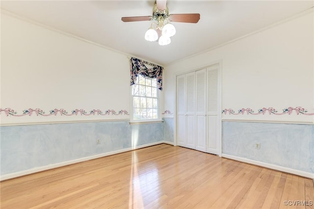 unfurnished bedroom featuring a wainscoted wall, a closet, a ceiling fan, wood finished floors, and baseboards