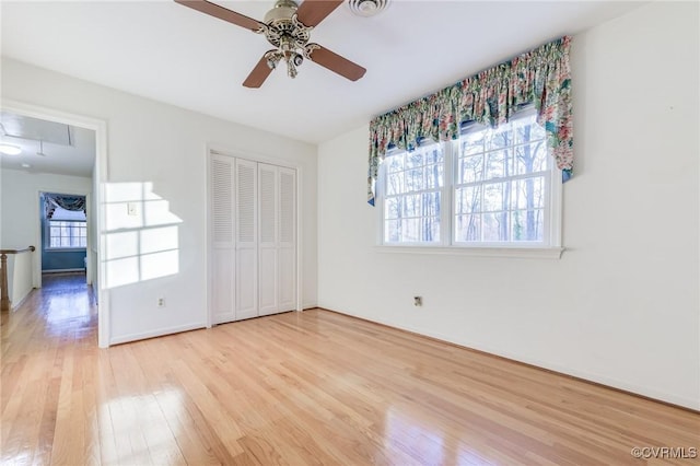 unfurnished bedroom featuring a closet, attic access, ceiling fan, wood finished floors, and baseboards