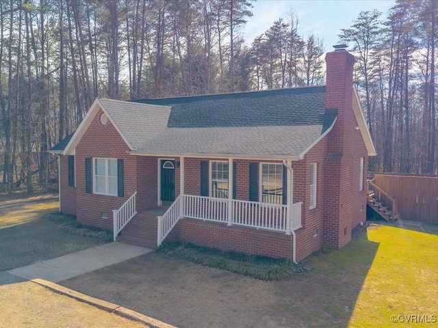 view of front of property with brick siding, a chimney, roof with shingles, covered porch, and a front yard